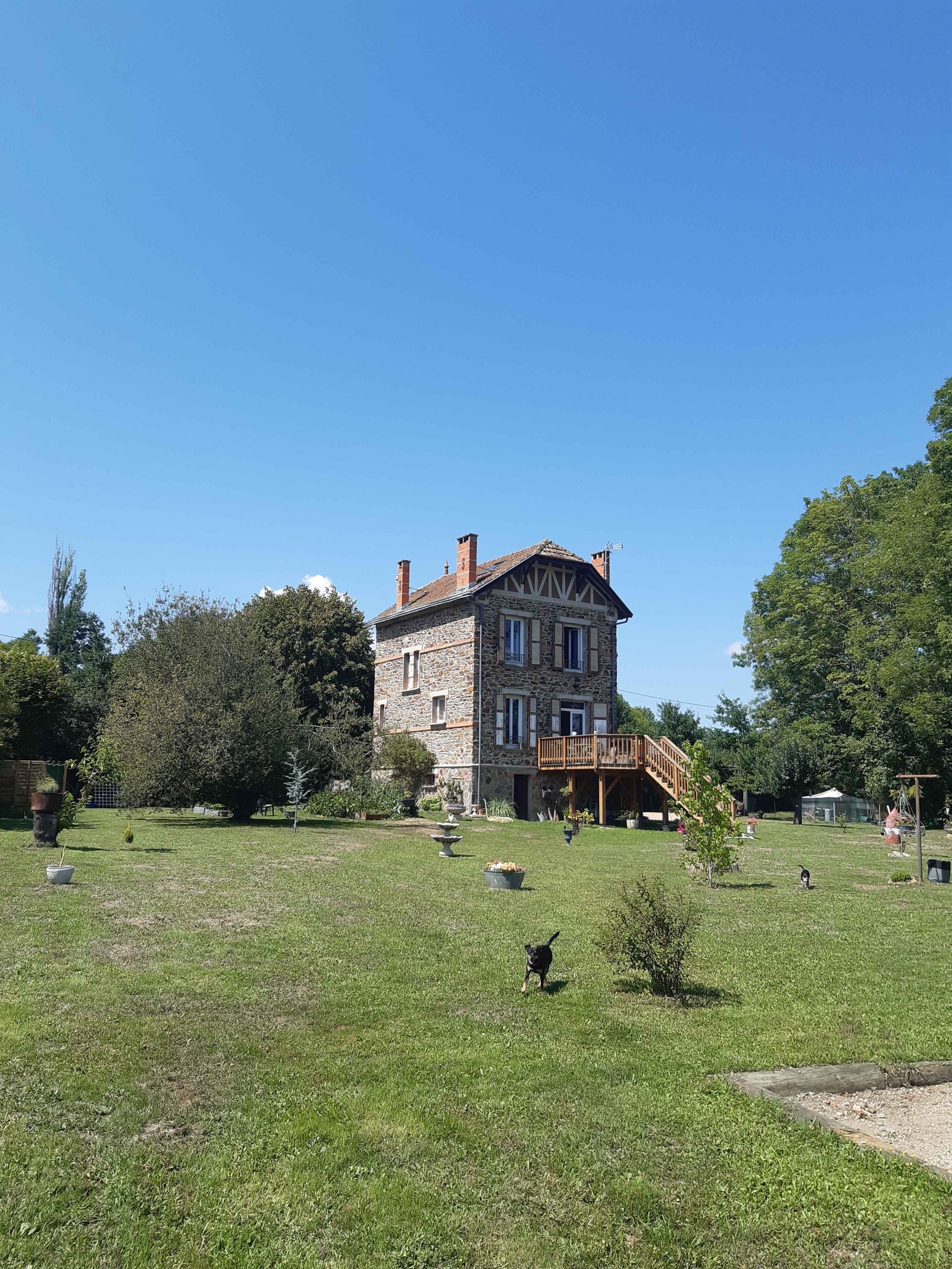Le grand terrain clos et la maison en pierre, avec un chien qui court sur la pelouse